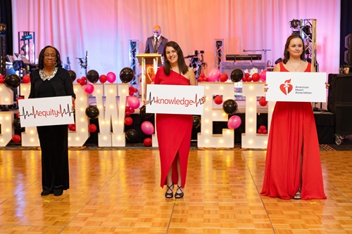 Three women on the dance floor holding signs reading equity, knowledge, and American Heart Association.