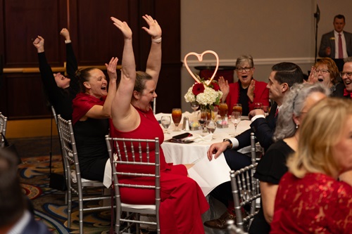 Table of guests celebrating by holding their hands in the air.