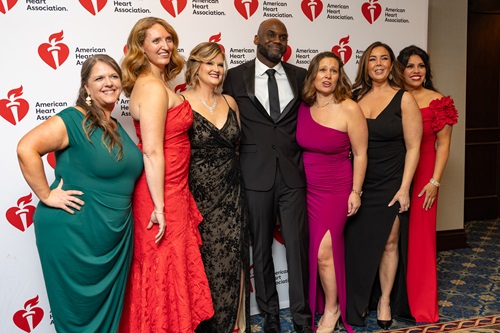 Group of seven people in formal attire in front of American Heart Association banner